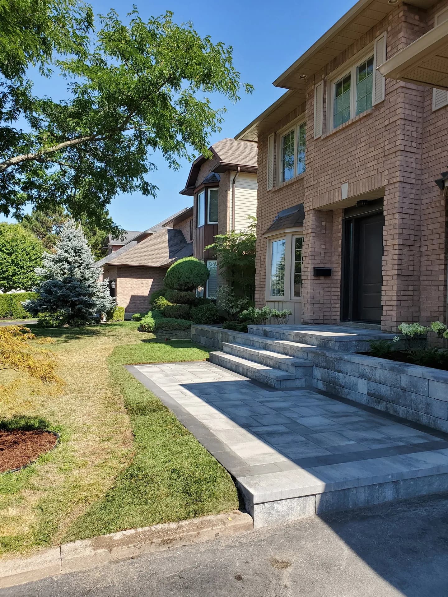 Interlock front entrance walkway and steps with charcoal border pavers leading from a driveway to a brick home in Hamilton, Ontario