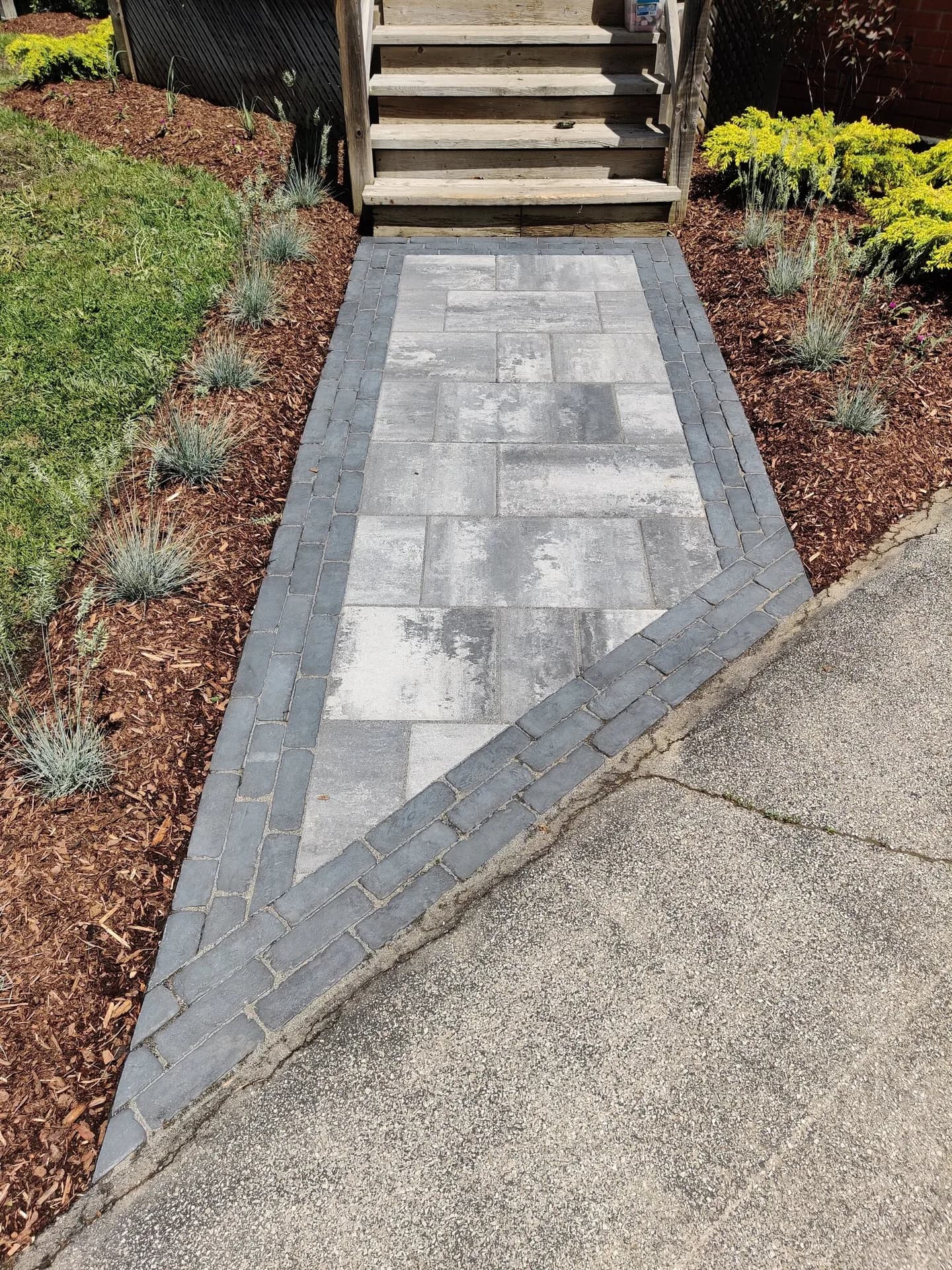 Interlock walkway installation with charcoal border pavers meeting an asphalt driveway at a residential entrance in Hamilton, Ontario