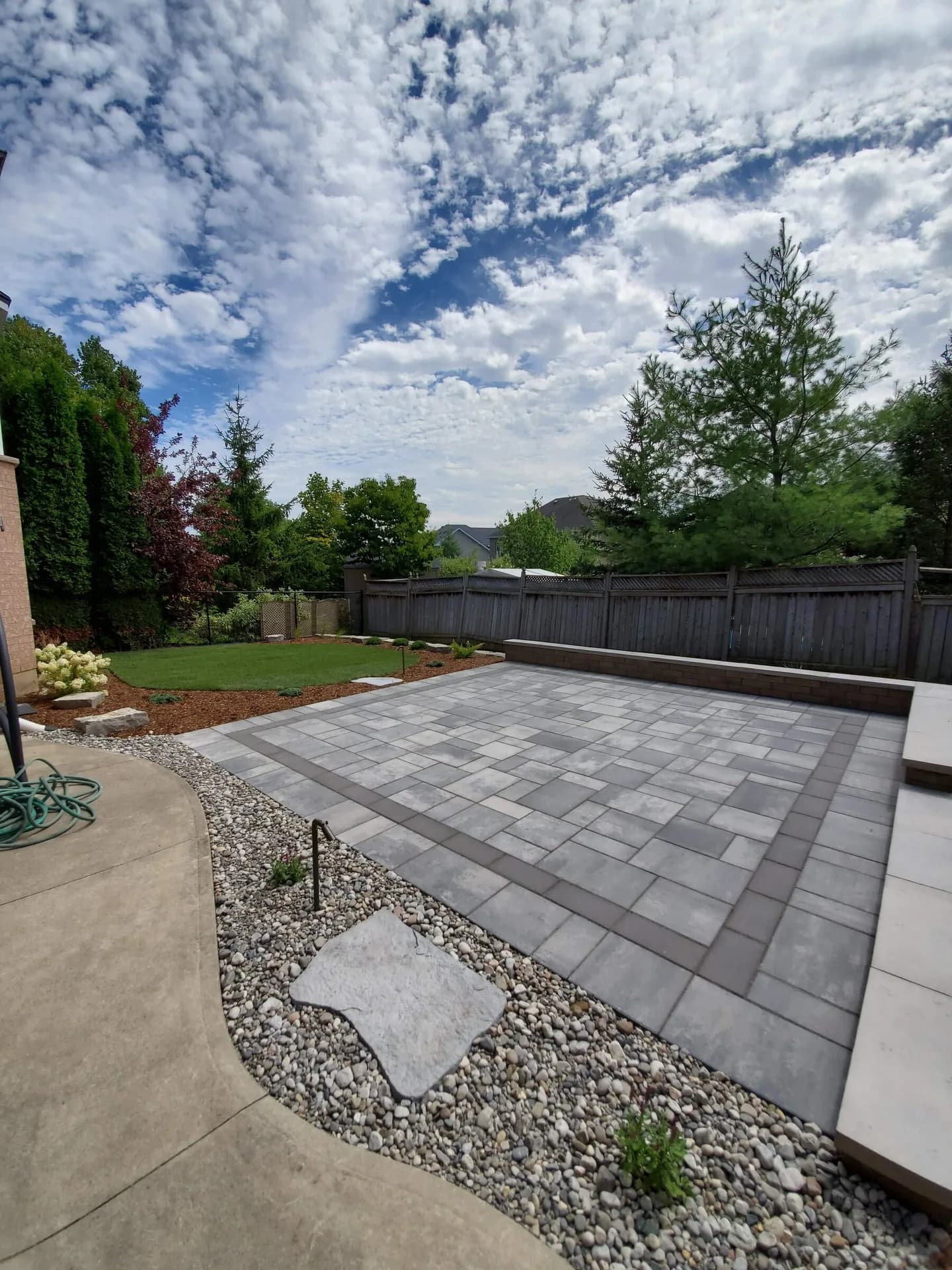 Interlocking patio installation with charcoal border pavers and stone seating wall in a residential backyard in Hamilton, Ontario