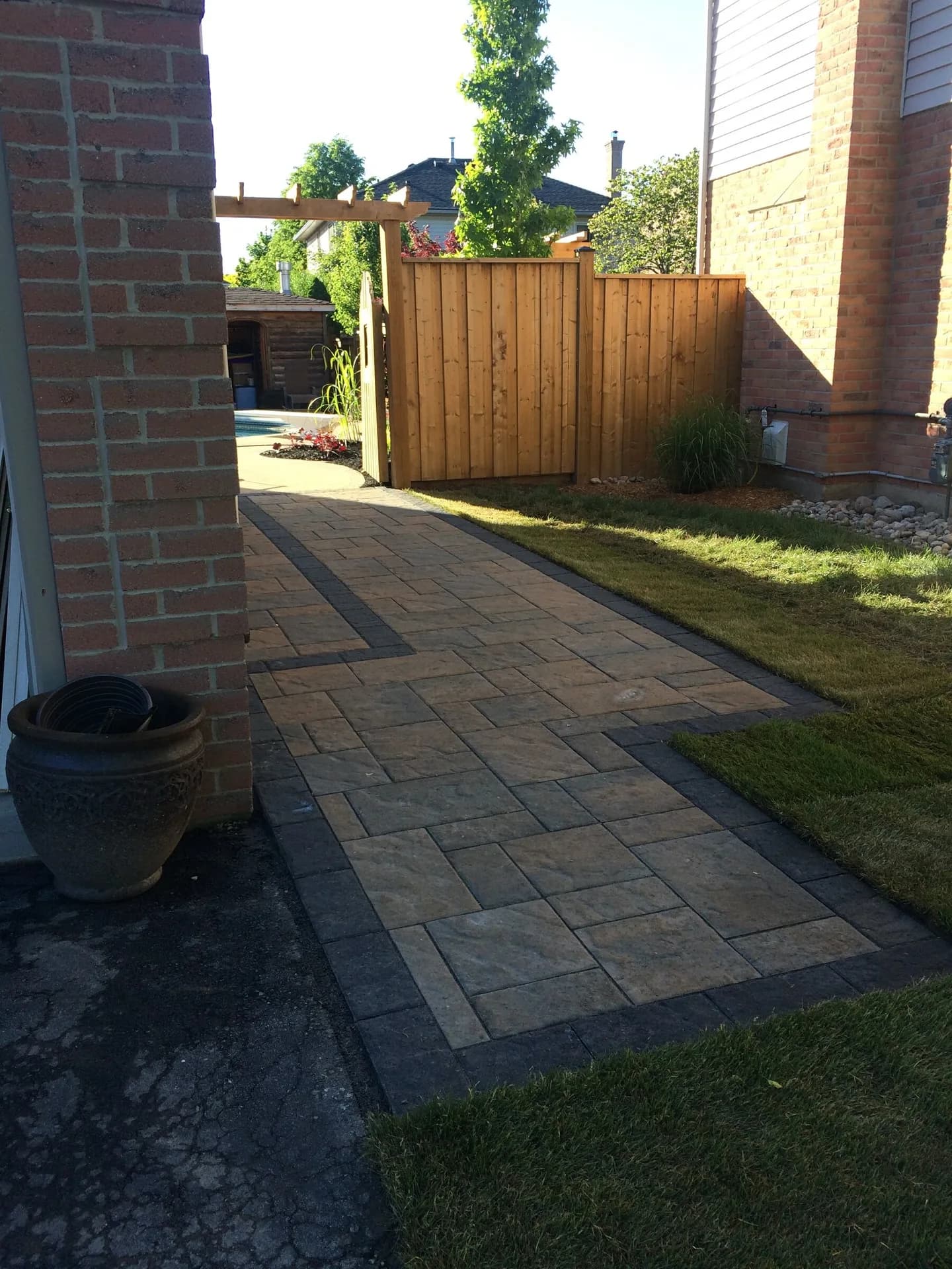 Side-yard paver walkway installation with charcoal border and fresh sod along a brick home in Burlington, Ontario