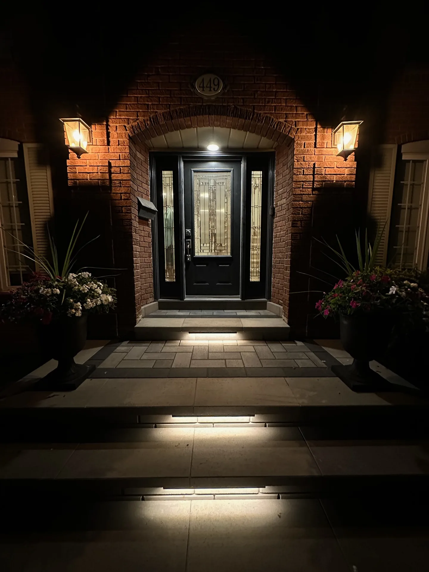 Outdoor landscape lighting with step lights, wall sconces, and entryway downlighting on interlock front steps in Hamilton