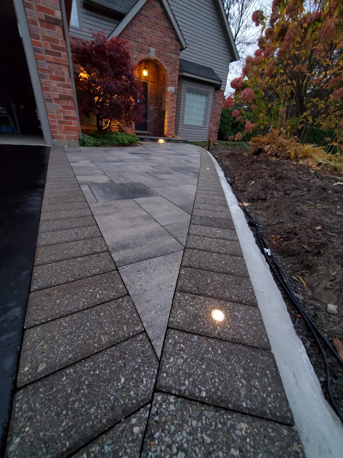 Landscape lighting installation with recessed LED lights built into paver walkway borders at a Hamilton area home at dusk