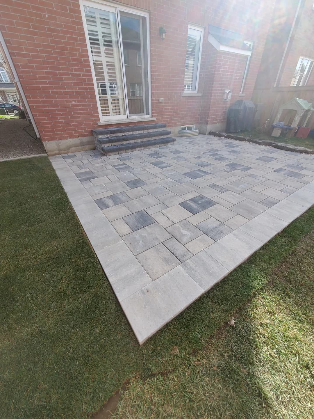 Grey interlock paver patio with charcoal border and stone steps at a residential landscaping project in Burlington, Ontario