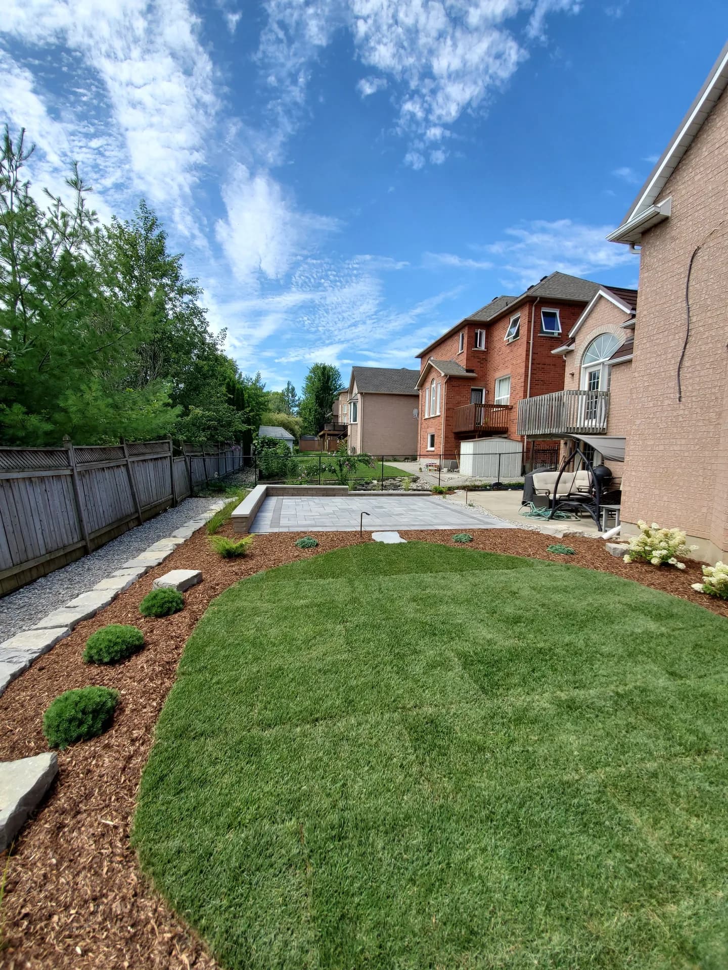 Sod installation in a Hamilton backyard with a curved green lawn bordered by mulch beds, shrubs, and a grey stone paver patio