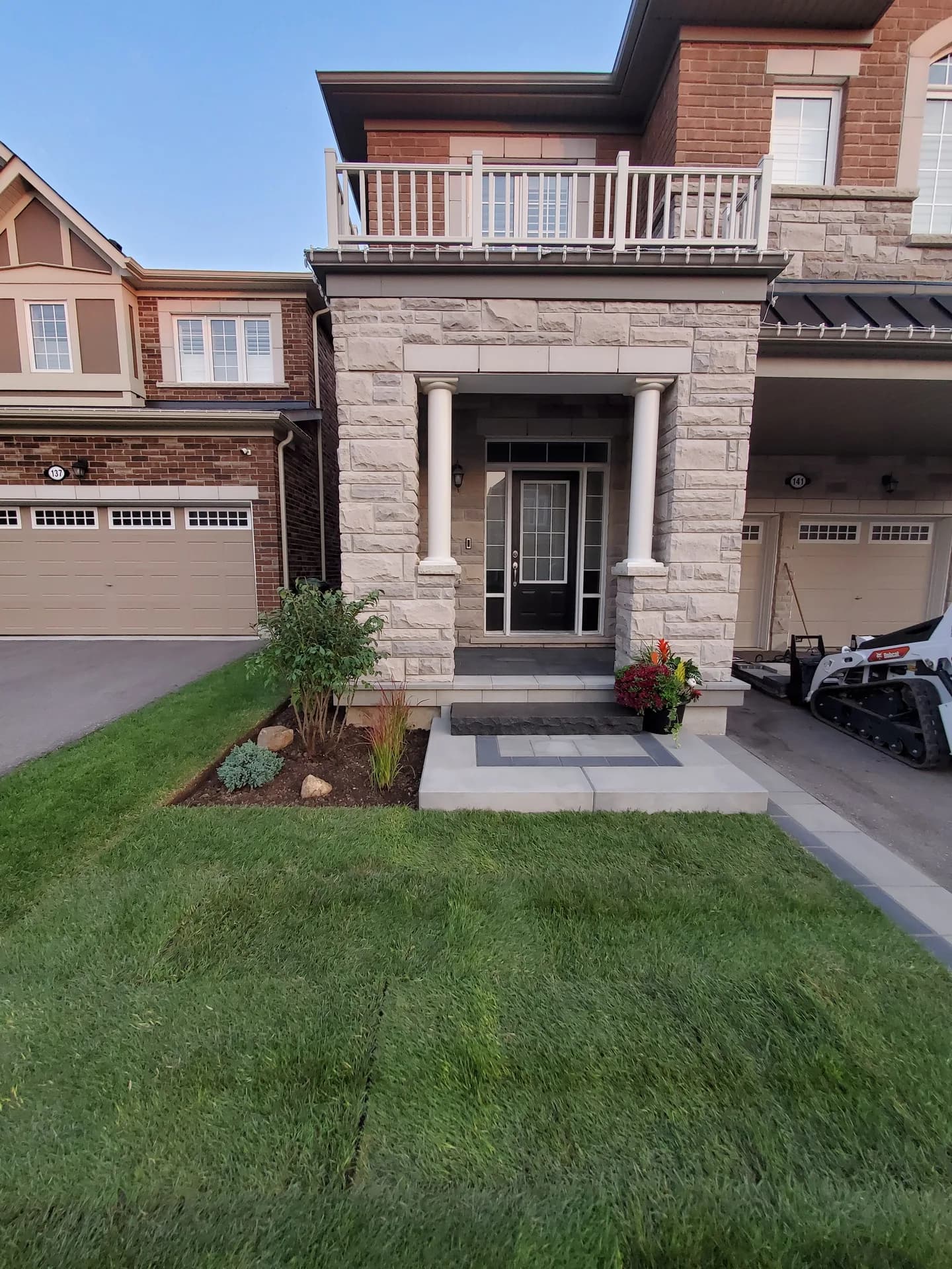 New lawn sod laid across a front yard in Hamilton beside a stone entrance with white columns and a paver walkway