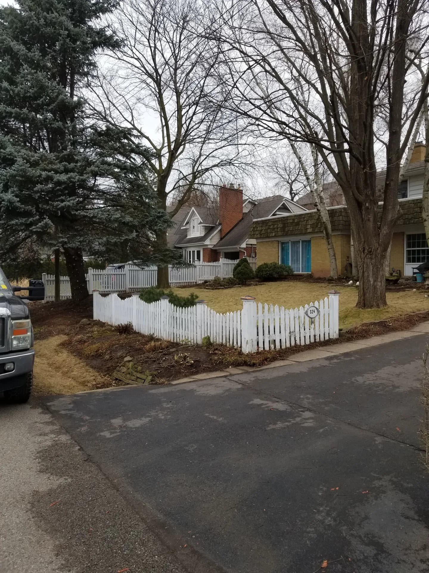 After spring yard clean up in Hamilton with trimmed shrubs, cleared garden beds, and a tidy lawn along a white picket fence